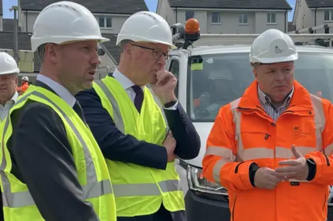 Two men in yellow hi vis and a man in orange hi vis in a residential street