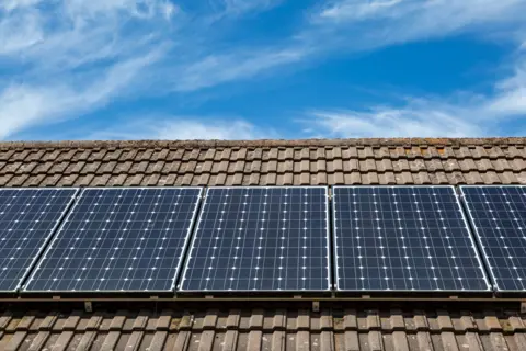 Black pannels on a brown tiled roof with a blue skye merged with light white clouds. 