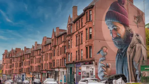 Getty A mural by the Australian artist Smug (Sam Bates) on a gable end of a tenement block in Glasgow's High Street depicting a modern interpretation of the city's saint, St Mungo, saving a robin.