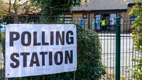 A white sign on a school fence indicating it is a polling station