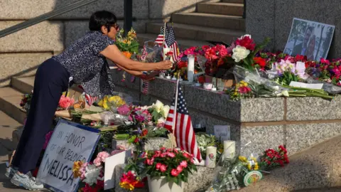 La bandera de la imagen de Getty y la pantalla de flores llenan la imagen mientras las mujeres se inclinan y colocan flores en el medio de la disposición