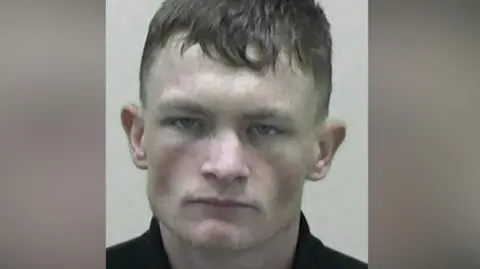 Mugshot of Shaun Hodgson. He has a menacing expression and is clean shaven with short dark hair.