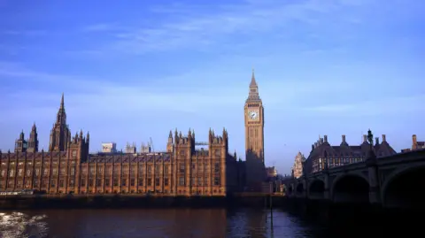 PA Media London's Houses of Parliament is lit up by the sunlight, against a backdrop of a blue sky. The River Thames and Westminster Bridge remain in the shadow. The time on Big Ben reads 8:35. 