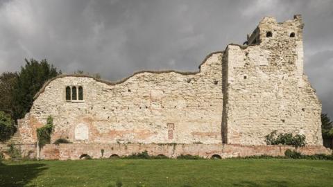 Wallingford Castle remains, featuring an old partial brick wall with some windows. In the foreground there is grass.