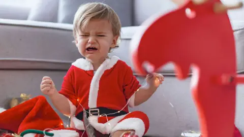 Getty Images Upset child in santa outfit with rocking horse crying