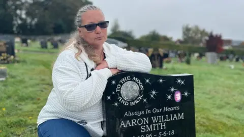 A woman crouches by her son's grave in Beeston cemetery