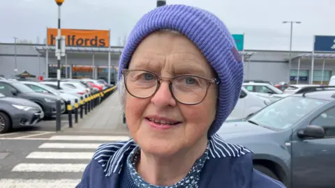 A woman wearing a purple hat and glasses looking at the camera