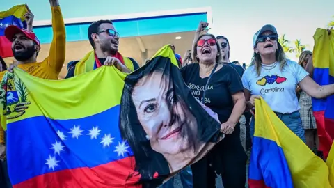 Getty Images Venzuelans holding a banner with the face of María Corina Machado at a rally in Doral on 3 January 2026. 
