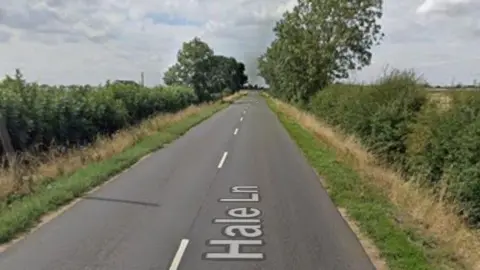 Google A Google image of a road heading through the countryside. There are open fields either side and a line of trees up ahead.