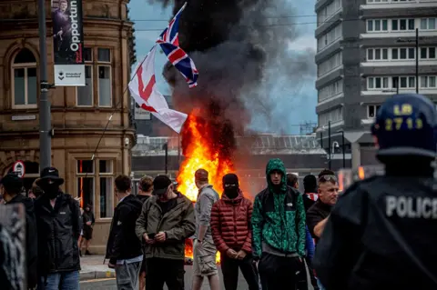 Getty Images Διαδηλωτές κατά της μετανάστευσης συγκεντρώνονται μπροστά από ένα φλεγόμενο Γραφείο Συμβουλών Πολιτών