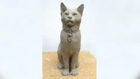 Handout Hendrix's statue at the workshop. He is sitting with a serious look and his ears perked up. He is wearing a pendant.