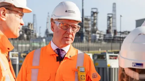 PA Media John Swinney in an orange high-visibility jacket and hard hat at an industrial plant 