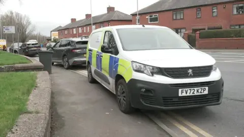 A yellow and blue liveried police vehicle is parked up on the kerb outside the house.