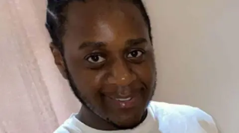 A close-up image of Jazmel Patterson-Low, wearing a white T-Shirt and smiling at the camera.