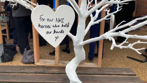 Cathy Minton/BBC A white tree and branches with a heart hanging with the wortds: 'For our NHS heroes who held our hands'