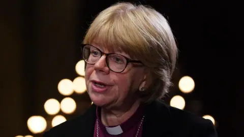 Dame Sarah Mullally, who has a blonde bob hairstyle with a fringe and wears glasses with a dark frame, is pictured speaking at a previous event at Chapter House in Canterbury Cathedral