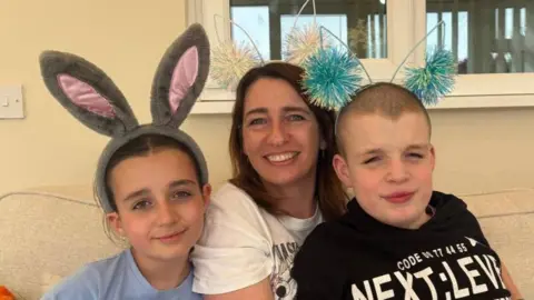 Contributed Sarah Saul sits on a sofa with William on her lap and daughter Amelia sat next to them. Amelia wears a large bunny headband on her head and William and Sarah wear headbands with white and blue ears with some pom poms on them. 