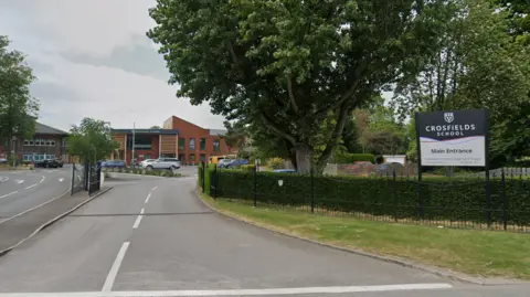 Google The entrance to a school, which has a navy and white sign outside reading "Crosfields School Main Entrance". It is fenced off with a gate. Beyond the gate are a number of brick school buildings.