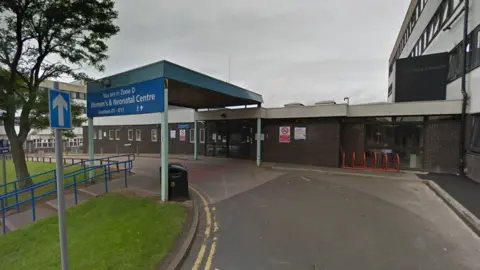 Exterior of the neonatal department at New Cross Hospital. A single-storey, flat-roofed building is in the foreground with an NHS sign at the front