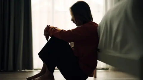 In silhouette of woman sitting on a bedroom