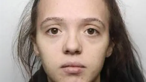 A mugshot of a woman with her brown hair in a ponytail.