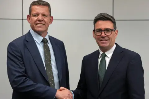PA Media Rhun ap Iorwerth shaking hands with Andy Burnham in front of a grey backdrop. 