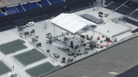 A drone shot shows a cover for a boxing ring being erected in the middle of the Portman Road stadium. A sheet has been placed over the pitch and rows of chairs placed on each side of the ring