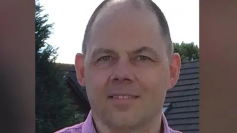 Chris Stockport, who has close cropped dark hair and is wearing a pink shirt.