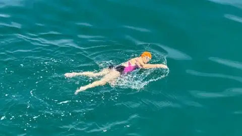 Cosmic Dot, who wears an orange swimming cap and goggles, swims in the channel.