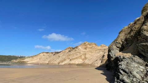 Bright blue sky behind cliffs with a sandy inlet in the foreground