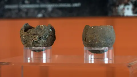 Martin Rowe/Peterborough Museum and Art Gallery Close up views of two Bronze Age pinch pots displayed in an exhibition case against an orange background at Peterborough Museum.