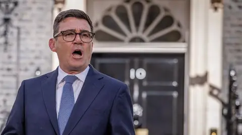 Andy Burnham in a navy suit and light blue tie speaks outside the black front door of 10 Downing Street in central London.