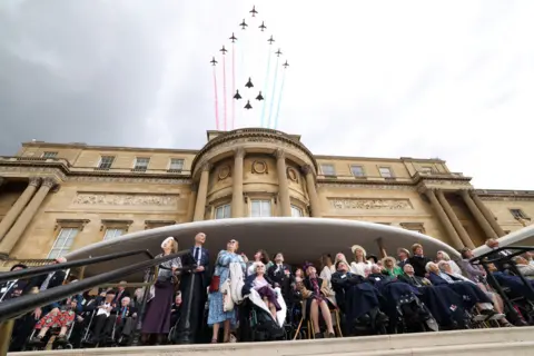 Reuters Second World War veterans and other guests look up at the sky as they watch the Red Arrows and other military aircraft fly over Buckingham Palace against a cloudy sky.