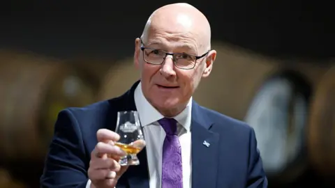 Getty Images John Swinney holding up a whisky glass towards the camera.