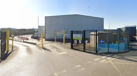 Google Images The image shows the outside of a recycling centre in Mole Valley. Some gates can be seen around the premises and a small blue sign with an arrow pointing inside.