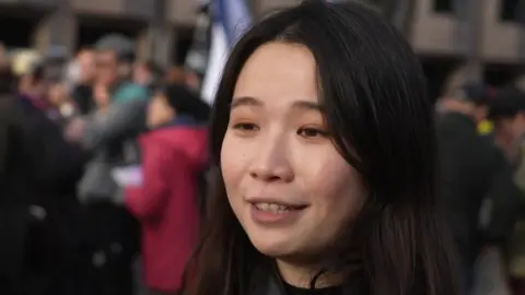 A young woman with long, dark hair standing in front of a crowd 