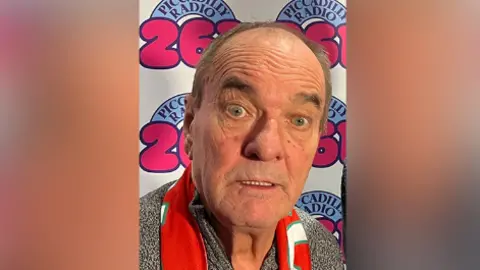 Pete Johnson Stannage as an older man in front of a radio backdrop 