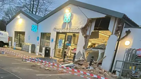 A Co-Op shop surrounded in police tape. Part of the front of the shop has fallen in, from top to bottom, with parts of the wall hanging off. 