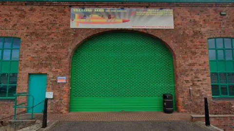 Google A brick building with door covered with a green metal shutter. A sign above the door reads "yellow sub on the docks" and has a picture of a yellow submarine with cartoon characters sitting on it