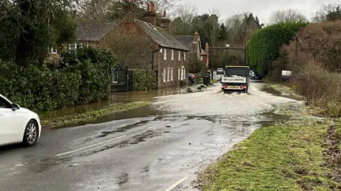 George Carden/BBC Flooding on the B2138 Lower Street Roadnear Fittleworth, West Sussex. A lorry can be seen driving through extensive rainfall on the road, which is flanked by houses to the left