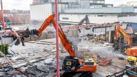 Bright orange specialist demolition equipment ripping down walkway