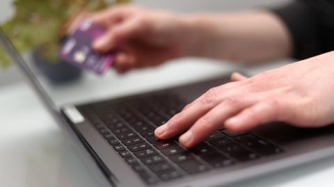 Woman using a laptop as she holds a bank card