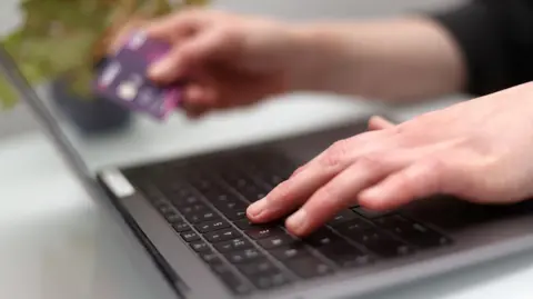PA Media Woman using a laptop as she holds a bank card