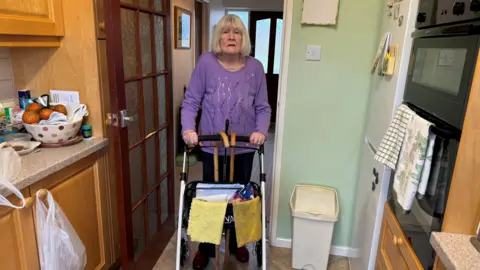 Woman standing in her kitchen holding onto her rollator.