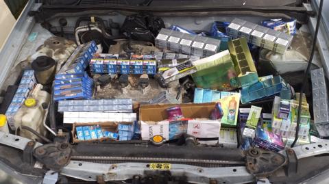 The engine compartment of a car filled with illegal cigarettes, tobacco and vapes