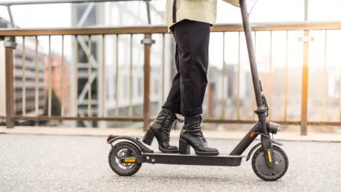 A woman rides an electric scooter on a city street.