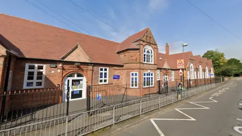 Google Maps A photo of a school in Erdington which is red brick and has triangle shaped roof. It has arched windows and a black fence round the front of the school. 