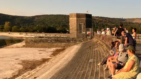 People are sat on stone steps looking at the sun