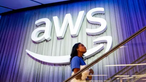 Getty Images A woman climbs the stairs in front of the giant AWS sign. It's the three letters AWS with an Amazon smiley arrow underneath it.