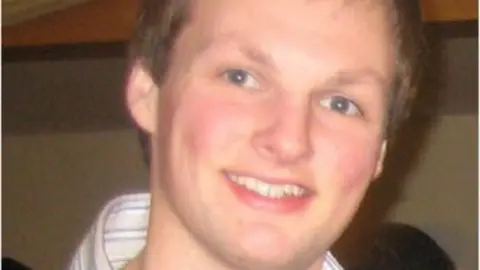 Shane O'Farrell has short blonde hair and blue eyes. In the close up picture he appears to be wearing a white stripped shirt.